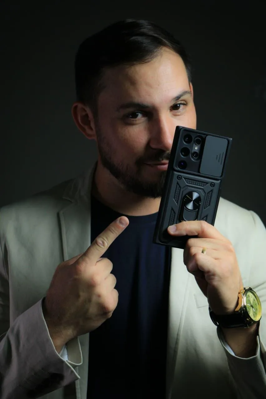 Luan Silva de blazer bege, apontando para as câmeras na traseira do celular